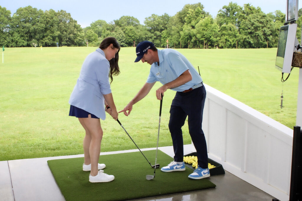 Male golf insuctor assisting female golfer at toptracer driving range