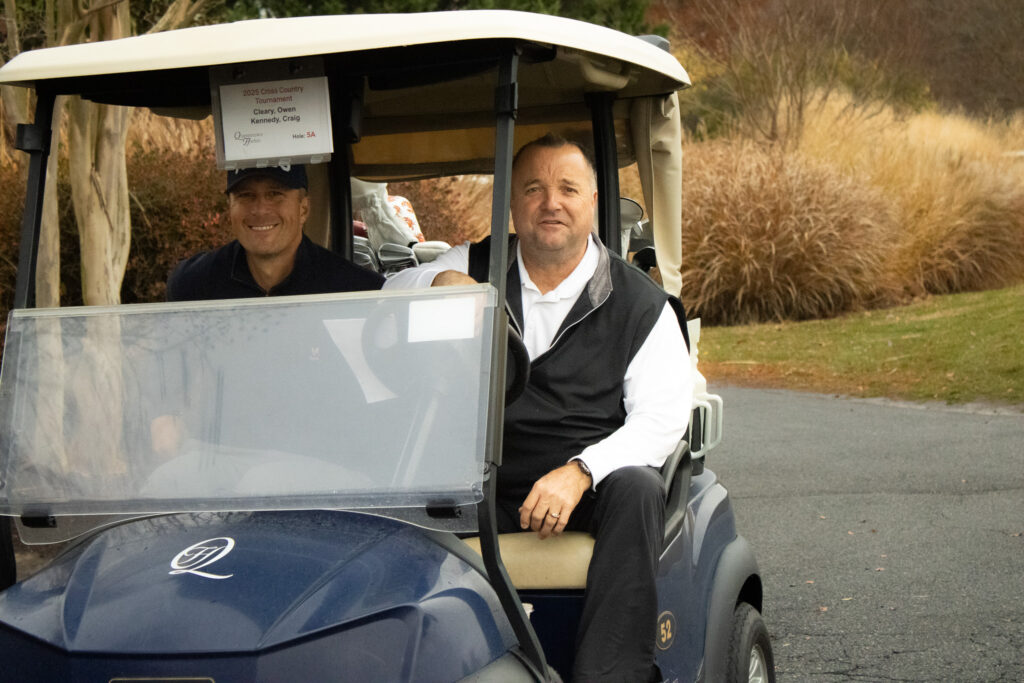 two men drive by in a golf cart at queenstown harbor