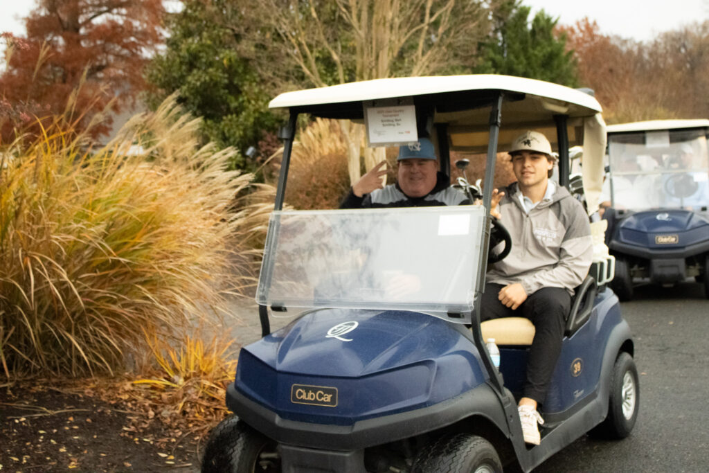 participants of the annual Queenstown Harbor Cross Country Tournament ride by in a golf cart