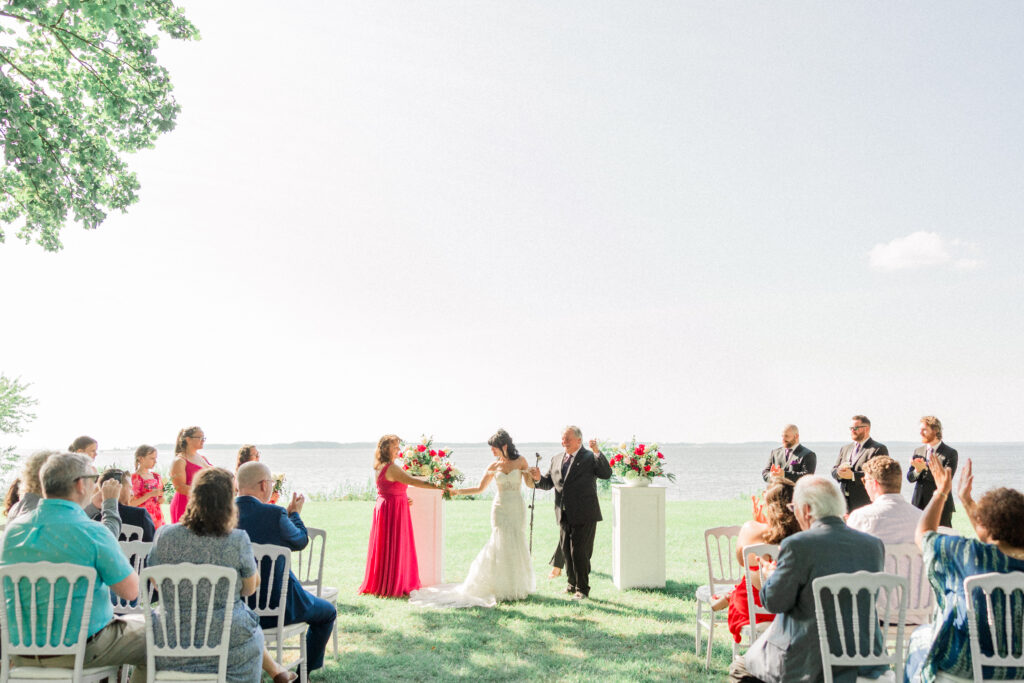 a bride and groom smile during their wedding ceremony at queenstown harbor on the eastern shore