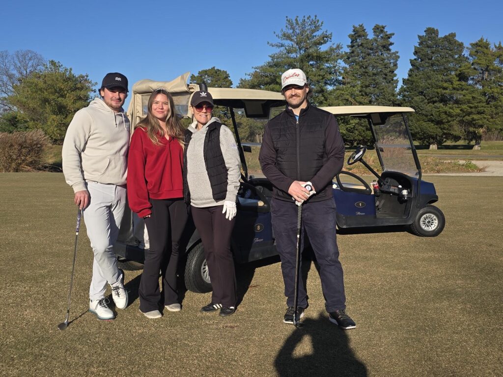 four golfers pose together in front of a golf cart at queenstown harbor
